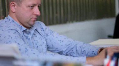 Erkek ofis çalışanı bilgisayarın başında oturmuş klavyeye konsantre olarak ofis patronu olarak çalışıyor. Pek çok renkli kalem, memnun olmayan bir bardakta yoğunlaşmıştı. ifade