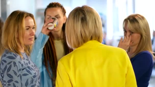 休憩中にオフィスにいる4人の女性は お茶のトークのゴシップを飲んで 企業パーティーのブロンドを祝う黄色い青い服を笑います 赤いドレッドロックと彼女の頭の休憩 — ストック動画