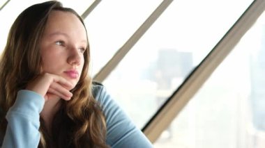 Genç bir kız pencerenin kenarında oturur, üzgün, çenesini eliyle kaldırır, makyajsız mesafeye bakar, ergenlik, ergenlik, psikolojik deneyimler, ilk aşk, kadın gözlerini kapatır, düşünür