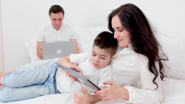 프리랜서로 일하면 아빠와 침대에서 컴퓨터 노트북으로 수있습니다 아들은 태블릿으로 놀면서 — 비디오