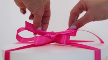 Beyaz bir kutunun üzerindeki yumuşak pembe kurdeleyi çözün. Kadın elleri, leylak rengi manikürlü yeni yıl kutlaması hediyesiyle. Yakın plan hoş bir doğum günü hediyesi. tatil
