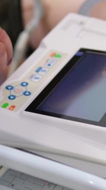 Hastanedeki kardiyogramda kadın doktor en son teknoloji makinesini kullanarak hastayı muayene ediyor ve göğsüne özel vakum bardakları koyuyor. Hastaya ekg yapar