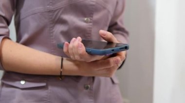 Cep telefonu elinde. Kadının eli cep telefonuyla yakın plan. Mavi eflatun çantalı, pembe üniformalı, hemşire. Tanınmayan insanlar mobil kablosuz internet ağı kavramını benimsiyor.