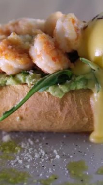 Lezzetli karides karidesli Benedict peynirli avokado ve yumurtalı tost. Parmesan yeşili iştah açıcı aromatik öğle yemeği aperatifi. Gri tabakta keten taneleri serpiştirilmiş. Restoran servisi