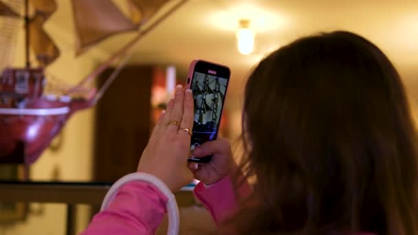 彼女の携帯電話のピンクのシャツのフィルムの若い女の子は レストランの博物館のリングにあるおもちゃの木製の船を横に見ているフランスのマニキュアホワイトハンドバッグティーンエイジャーの少女 ソーシャルネットワークの撮影 — ストック動画