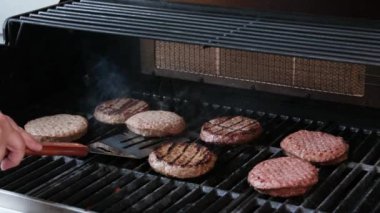 Tepesi aşağıda, ızgarada pişen hamburgerleri yakından izleyin. Birisi hamburgerleri çeviriyor ve alevler yükseliyor. Yüksek kalite 4k görüntü
