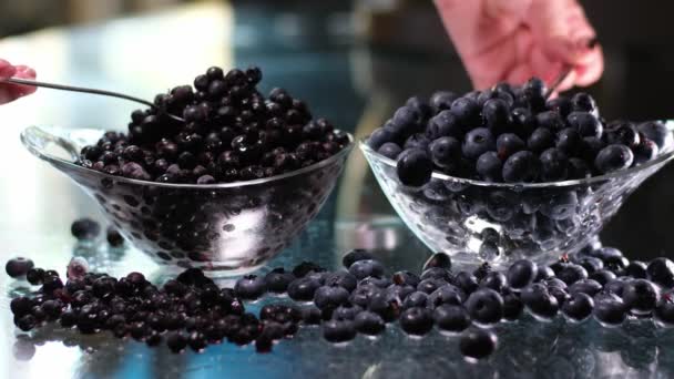 蓝莓和蓝莓的比较大的覆盆子从玻璃杯中取出 用勺子蓝莓把汤匙撒在玻璃桌上 之间的差异 — 图库视频影像
