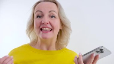 Güzel, orta yaşlı, elinde telefonla el sallayan el sallayan el sallayan, kameraya bakan, yanağına tokat atan, iyi haberi şaşırtan, içeriğinin reklamını yapan hoş bir kadın. Metin için boşluk