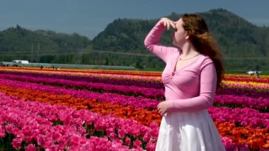 Pembe elbiseli ve hasır şapkalı genç kız lale tarlasında dikiliyor. Bahar geldi.