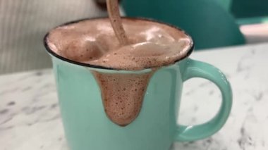 Sıcak kakao içeceği, altın kaşıkla karıştırılmış yeşil seramik bardak köpüğünün üzerinde akıyor. Ev istirahatı için sıcak bir Noel akşamı yakın plan çikolatalı içecek. zevk