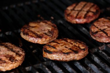 Izgarada, mangal kömürü ve taze köftelerle barbekü için ev yapımı burger arkaplanı oluşturan yarım kızarmış köfteler var. Mangalda ateşte pişen hamburgerler.