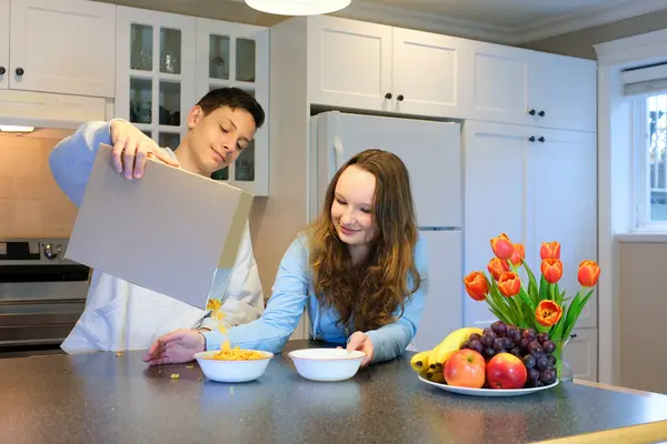 Loving daughter help mother and brother prepare breakfast before school. Healthy eating at home. Pleased teen girl pulls bottle of milk out of fridge for cornflakes. Happy family morning