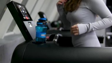 Sulu spor kadın portresi. Güzel, güçlü, kaslı bir kadın spor salonunda su içiyor. Gri spor kıyafetli genç bir kadın ve bir şişe su. İnce jimnastikçi merdivenlerde oturuyor. Yüksek kalite