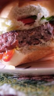 Isırılmış burger, lezzetli kahvaltı, öğle yemeği, bir ısırık al, kırmızı domatesi peynirli hamburgerin üzerine koy. Yüksek kaliteli FullHD görüntüler