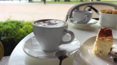 Şeftalili turta, browni, kurabiye ve küçük bir porselen tabakta cheesecake 'in küçük parçalarını yakın plan çek. Tabağın yanında parlak bir çatal var ve hepsi bir fincan sütlü kahveyle servis ediliyor..