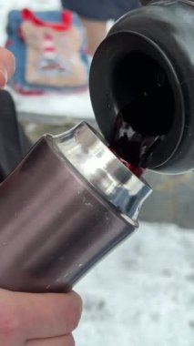 Sıcak çayın kışın termostan metal bardağa buharla dökülmesine yakın. Sıcak giysili kadın gezgin, soğuk ve güneşli bir sabahta elinde kaynar suyun kapağını tutuyor. Yüksek kalite 