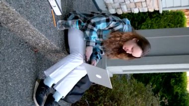 Kız üniversite öğrencisi kulaklık takıyor. Akıllı telefon uygulaması kullanıyor. Merdivenlerde oturuyor. İnternette öğreniyor.