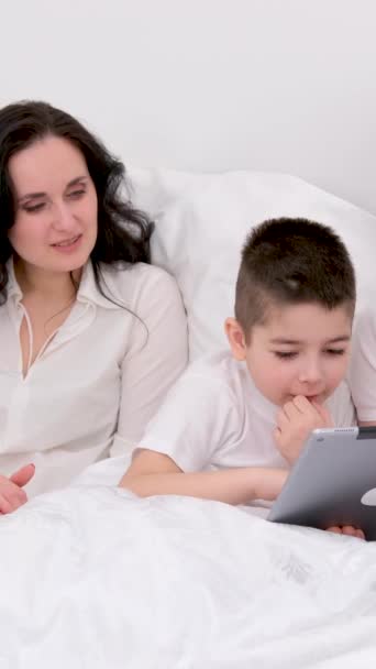 小さな息子とベッドの中の夫妻タブレット漫画を見て面白いゲーム写真笑っている通信本当の人々にホーム愛の生活幸せな家族生活喜びの人々白の背景 — ストック動画