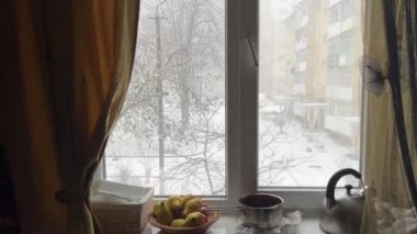 Mutfak penceresinden sokağı gören çok katlı evler, kışın pencere eşiğine kar yağıyor, armut çaydanlığı. Evdeki gerçek insanların sıradan hayatı, soğuk sokakların manzarası.