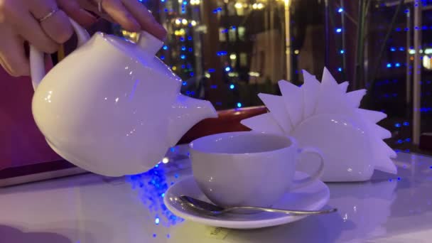 圣诞晚会上 在一家新年咖啡店里的茶壶里 盛满了美味的热茶 还有白桌餐巾 都是城市里的灯火通明的窗口餐厅 带戒指茶匙的女性手 — 图库视频影像