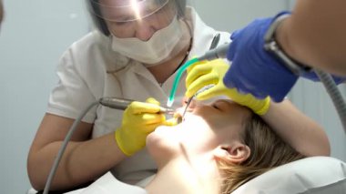 Kadın hasta diş muayenesi sırasında ağzı açık bir şekilde stomatoloji sandalyesinde oturuyor. Diş ağrısını kontrol eden erkek diş hekimi diş hekimliği ekipmanı kullanıyor.