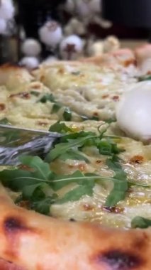 Kadınların elleri pizzacıda paten bıçağıyla bir dilim sıcak pizza kesiyor. Yakın plan. Dört peynirli pizza roka ve mozzarella ellerle koparılmış peynir yakın plan fırında lezzetli