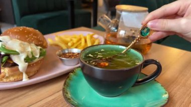 Dekoratif sofra takımı altın çay kaşığı zümrüt çayı arkaplan burger, çizburger, patates kızartması yeşil fincan ve çay tabağı öğle yemeği, akşam yemeği aristokratik yemekler. fast food