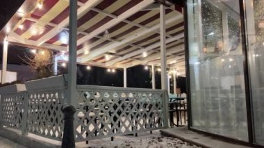 Kar gecesi parkı. Şehir parkına kar yağıyor. Yalnız bir kar kaplı bank denizin yanında duruyor. Noel Kış Yeni Yıl Manzarası. Kar yağdıktan sonra şehirde soğuk kış. Yüksek kalite