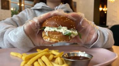 Genç aç kadın büyük hamburgeri ısırıyor. Fast food kafede hamburger yemek, yakın plan. Yüksek kalite 4k görüntü