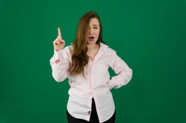 Yeşil arka planda pembe güneş gözlüğü takan heyecanlı genç bir kadın parmağını kaldırıyor. Yüksek kalite fotoğraf