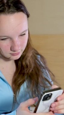 Genç bir kız yatağa oturur telefona bakar gri lekeli beyaz bir kutu saçlarını düzleştirir. 
