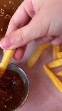 Lezzetli patates kızartmalarını domates sosuna bandıran kadın, yakından.