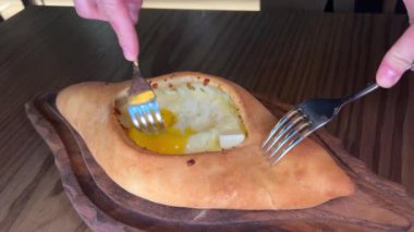 Gürcistan Adjarian Khachapuri Hand 'de suluguni peyniri ve yumurta sarısını karıştıran kişi. Adjarian Khachapuri' nin malzemelerini restoranda çatalla karıştırıyor. Peynirli ve yumurtalı turta. Çok lezzetli.