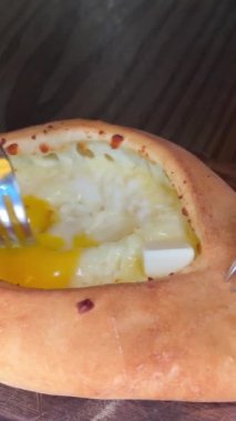 Gürcistan Adjarian Khachapuri Hand 'de suluguni peyniri ve yumurta sarısını karıştıran kişi. Adjarian Khachapuri' nin malzemelerini restoranda çatalla karıştırıyor. Peynirli ve yumurtalı turta. Çok lezzetli.