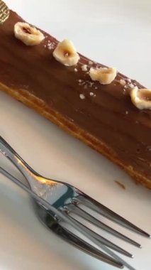 Bıçak ve çatal tomarının etrafında altın rengi ve fındık parçalarıyla beyaz tabakta nefis bir ekinedir. Lezzetli tatlıya bakar, sütlü çikolata serpiştirir. Yami servisi.