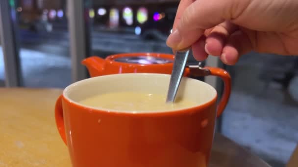 在冬夜的城市橙色的背景下倒入奶茶 茶壶杯靠近窗户的行人 经过汽车 不认识的人伦敦红茶加牛奶和糖甜 — 图库视频影像