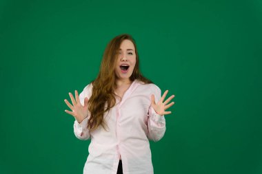 Şok olmuş genç bir kadın yeşil arka planda pembe bir bluz giyerken bir tarafa bakıyor. Yüksek kalite fotoğraf