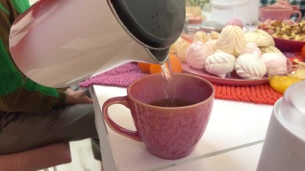 タンジェリンマシュマロとナッツティーパーティーパーティーの背景にピンクのカップに沸騰した水を注ぎ 大きなカップを閉じた女の子のテーブルシルエットでリラックス リラックスしたコミュニケーション — ストック動画