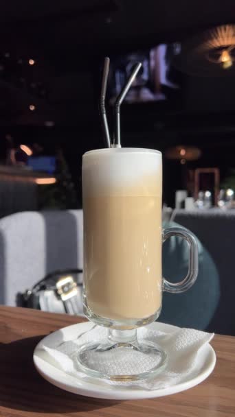 カフェの木のテーブルの上に立っているガラスのコーヒーのカップ コーヒーに関するリーフラテアート コーヒーショップで大豆ミルクでビーガンドリンク 4Kについて 高品質で — ストック動画