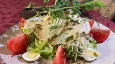 Sezar salatası croutons mikroyeşil bezelye domatesleri beyaz tabak üzerinde kırmızı masa örtüsü bir restoranda bıldırcın yumurtası marul ve sos bir restoranda yenir. çatal bıçağı