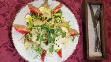Sezar salatası croutons mikroyeşil bezelye domatesleri beyaz tabak üzerinde kırmızı masa örtüsü bir restoranda bıldırcın yumurtası marul ve sos bir restoranda yenir. çatal bıçağı