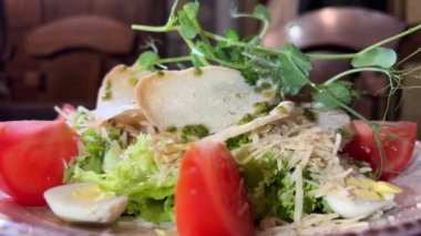Sezar salatası croutons mikroyeşil bezelye domatesleri beyaz tabak üzerinde kırmızı masa örtüsü bir restoranda bıldırcın yumurtası marul ve sos bir restoranda yenir. çatal bıçağı