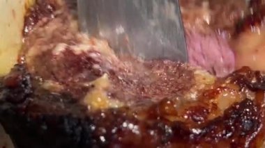 bbq, kebap büyük bir parça sulu eti büyük bir bıçakla kesti. Küçük demir spatula yağıyla tabaktan çıkarıyorlar. Kan akıyor.