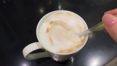 Sabah kahvesini karıştırır kaşık, karıştırılmış kapuçinoyu kalın süt köpüğüyle kaplar. Yüksek kalite 4k görüntü
