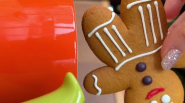 Zencefilli kurabiyeli Noel yemeği, bisküviyi bir fincan kahveye bandıran bir elin yakın çekimi meyveli kek ve kurabiyeler, ve göz kırpan geyik süslemeleri.