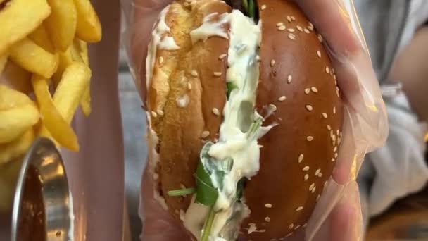 飢えた若い女性がビッグハンバーガーを噛んでいる ファーストフードカフェでハンバーガーを食べる クローズアップ 高品質の4K映像 — ストック動画