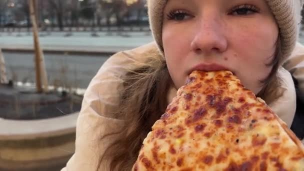 冬の女の子のストリートフードは ハットのクローズアップルーマニアブカレストイタリア旅行でストリートガールにピザを噛みます ランチ — ストック動画
