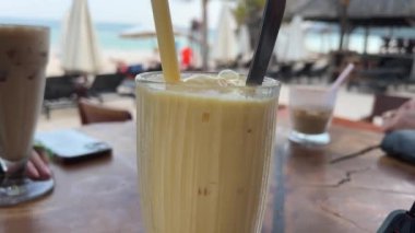 Mango Smoothie Lezzetli buzlu latte kahve Yazın deniz kenarında. Sahildeki kafede soğuk bir şeyler içelim. Seyahat et ve Bali adasının tadını çıkar. Yüksek kalite 4k görüntü