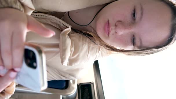 若い少女ティーンエイジャー乗り輸送で テキストスカイ列車のバスカーの通常の人のための窓ヘッドフォン携帯電話平和的な顔スペースを見ます — ストック動画