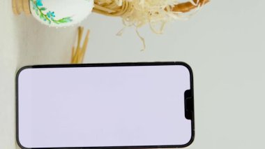 Paskalya bayramı telefonu reklam için boş bir yeri işaret ediyor. Sepet yumurtalarında yumurta desenli işlemeli kurdele yumurta kabuğu buğday çivileri ve hamur sepeti yakın çekim yeri.
